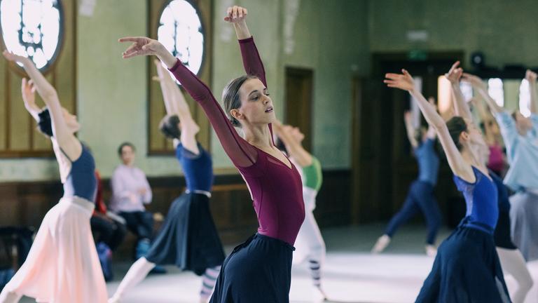 "L´Opéra - Dancing in Paris": Aurore (Hortense De Gromard) tanzt konzentriert in einem Ballettsaal inmitten einer Gruppe Balletttänzerinnen eine Figur.