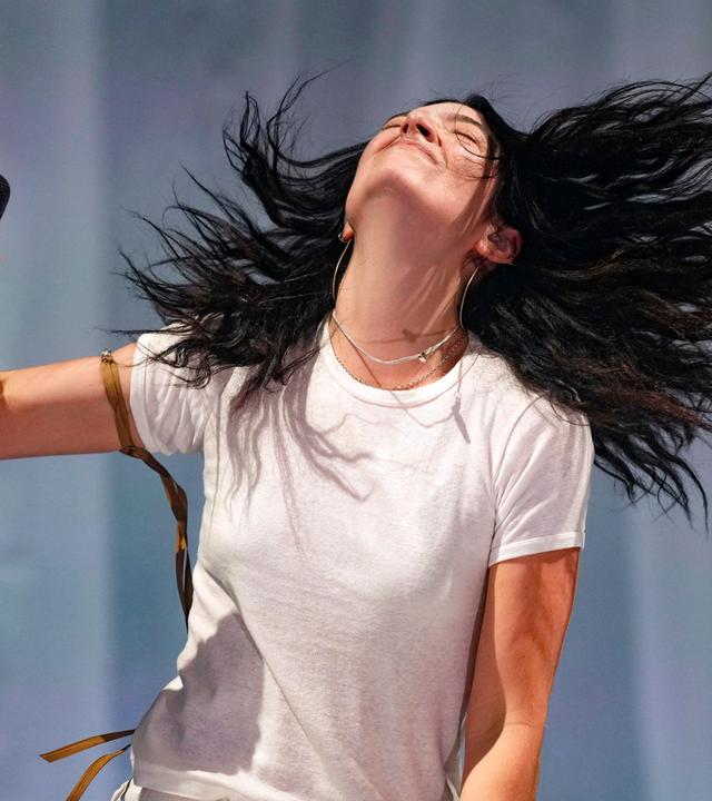 Eine Frau mit dunklen langen Haaren Hält ein Mikrofon in der Hand und schüttelt ihre lange Mähne.