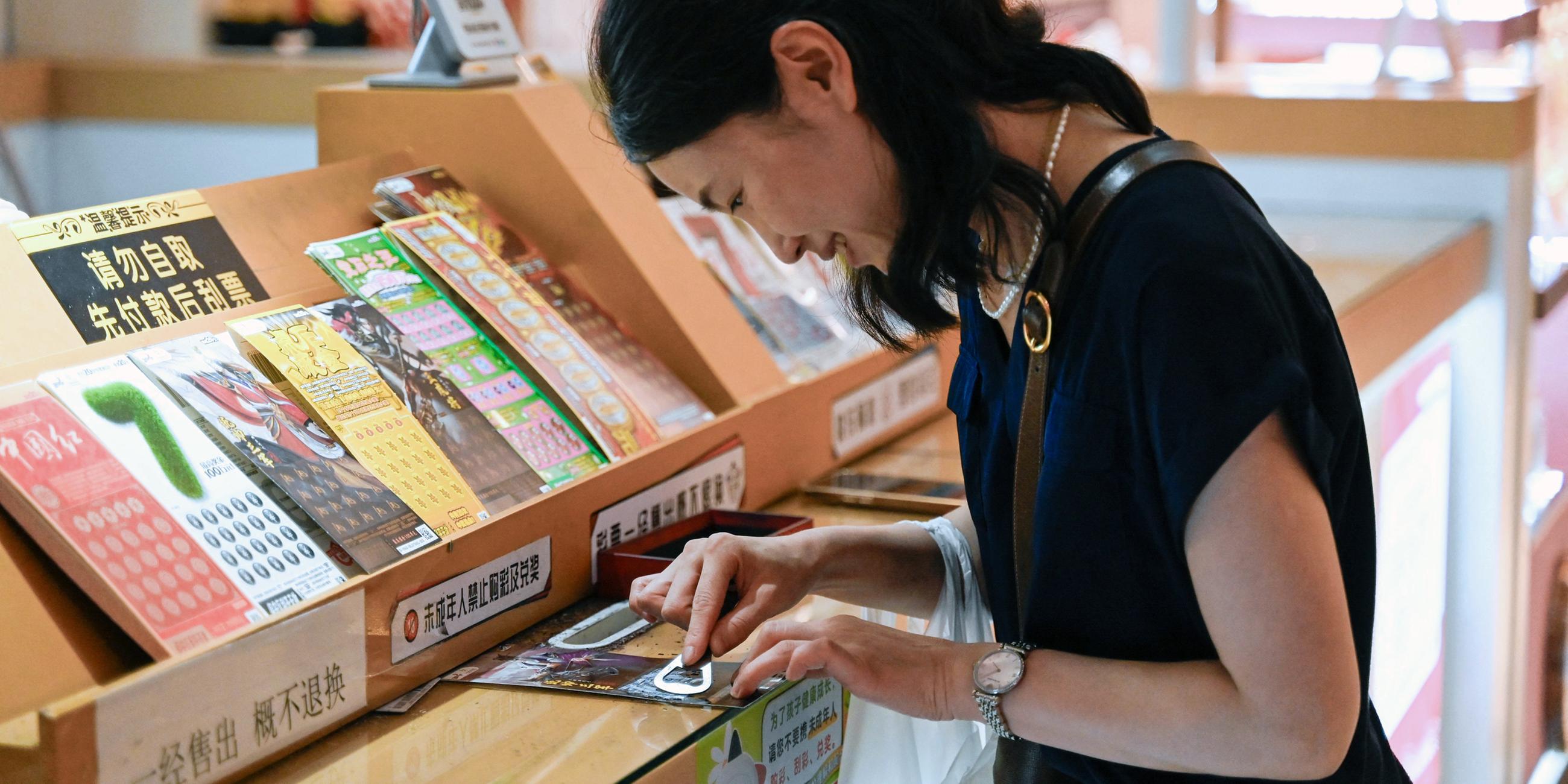 Frau, die an einem Stand in Peking einen Lottoschein aufrubbelt