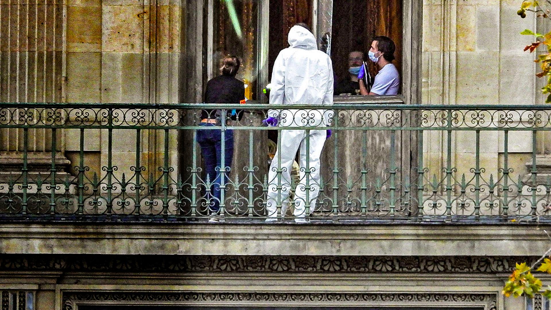 Vier Personen, davon eine im weißen Schutzanzug, stehen nach dem Einbruch in den Louvre auf einem Balkon des Gebäude.