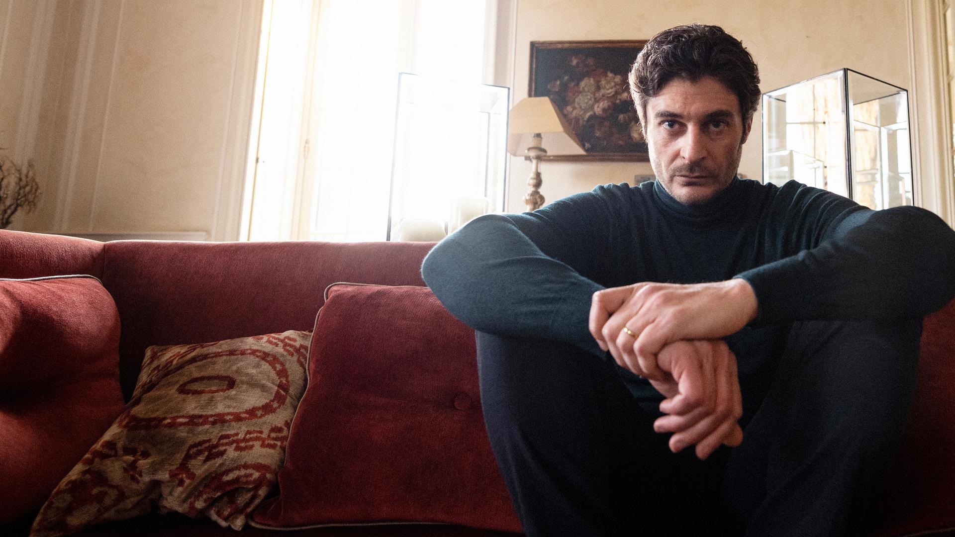 "Survivors": Luca (Lino Guanciale) sitzt auf seiner Couch in seinem Wohnzimmer und schaut sehr nachdenklich vor sich hin.