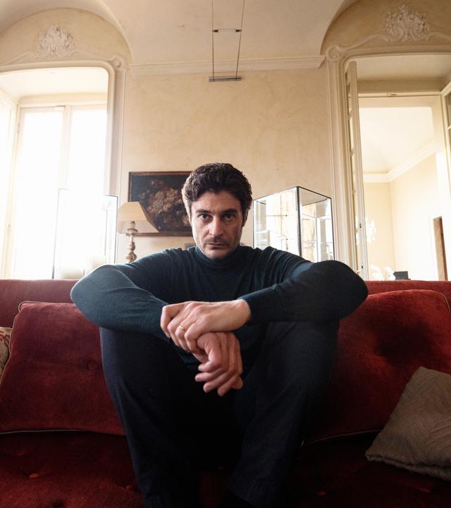 "Survivors": Luca (Lino Guanciale) sitzt auf seiner Couch in seinem Wohnzimmer und schaut sehr nachdenklich vor sich hin.