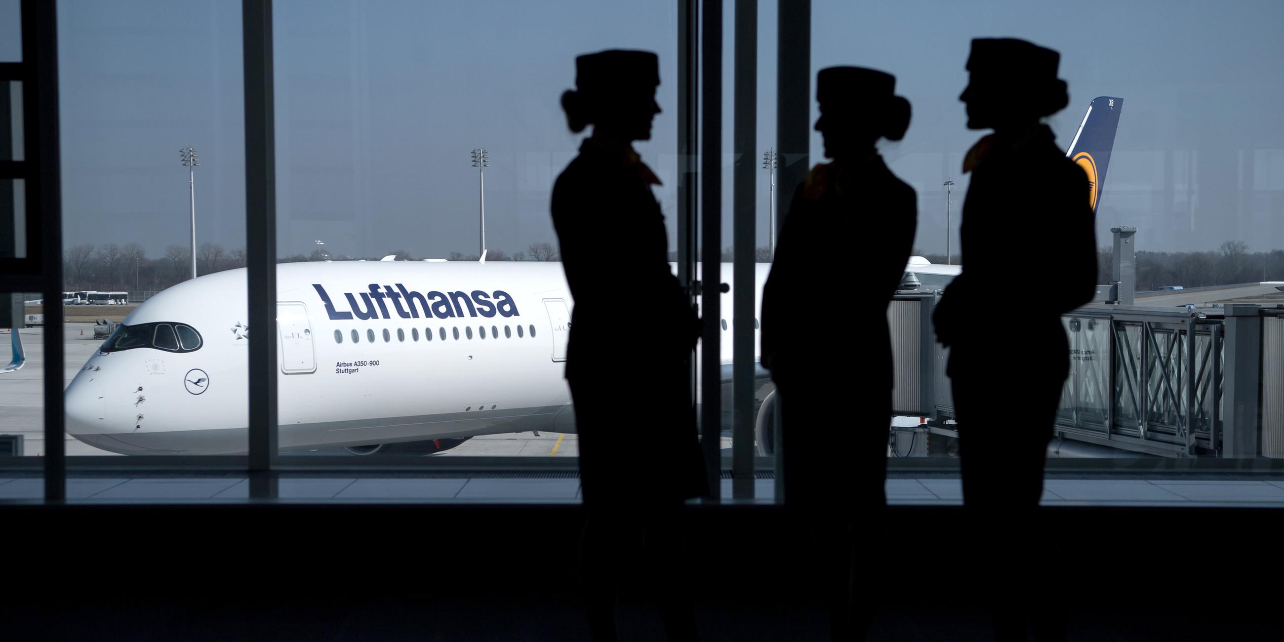 Flugbegleiterinnen der Lufthansa stehen vor einem Fenster am Münchner Flughafen. 