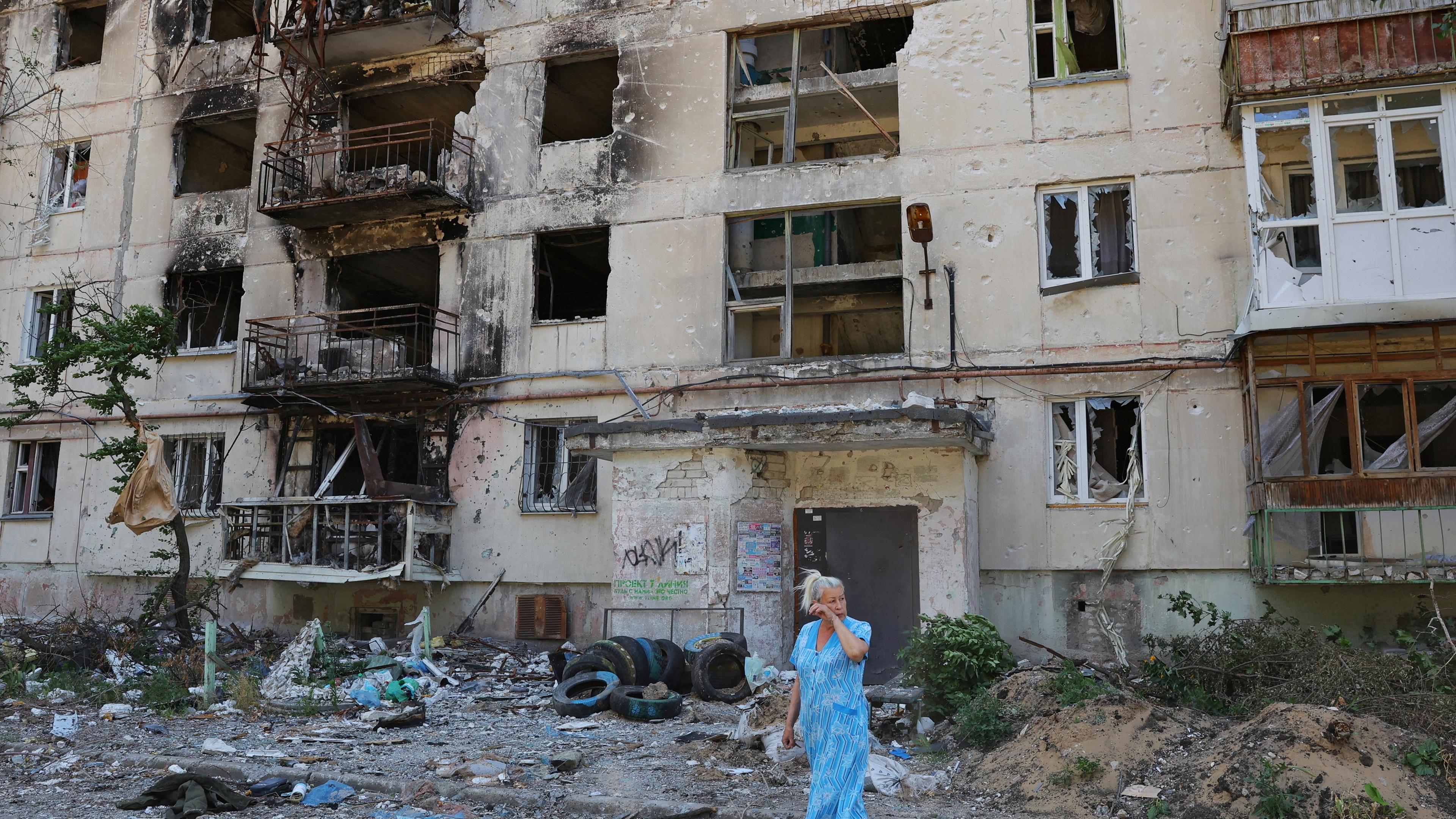 Eine Frau steht vor einem zerstörten Hochhaus.