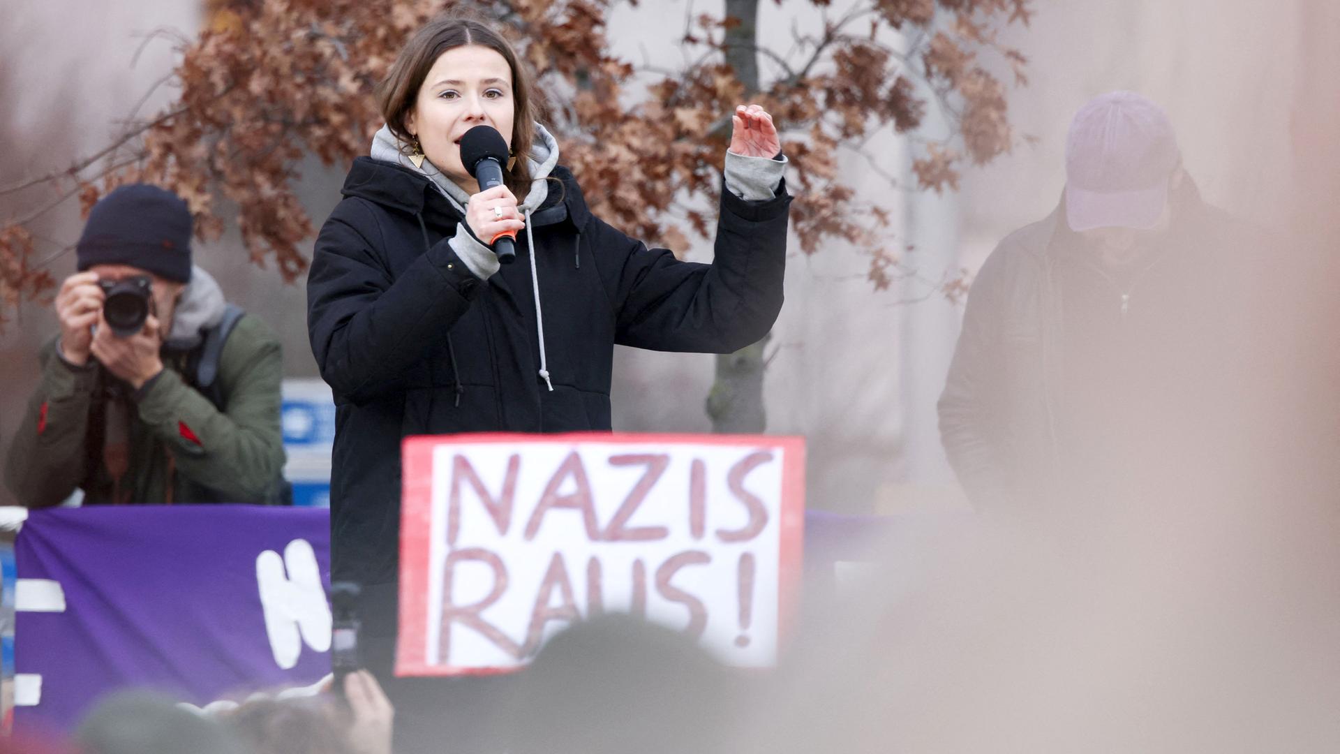 Frau mit Mikrofon, davor Plakat "Nazis raus"