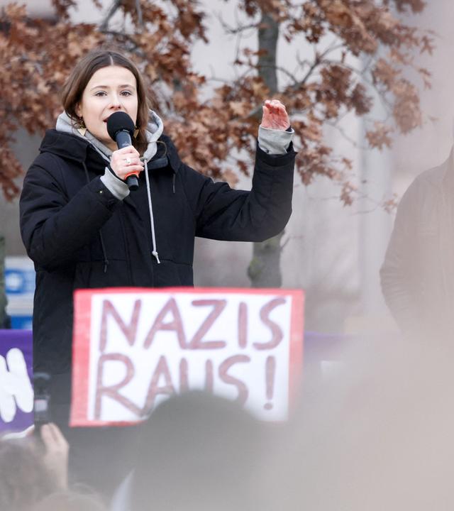 Frau mit Mikrofon, davor Plakat "Nazis raus"