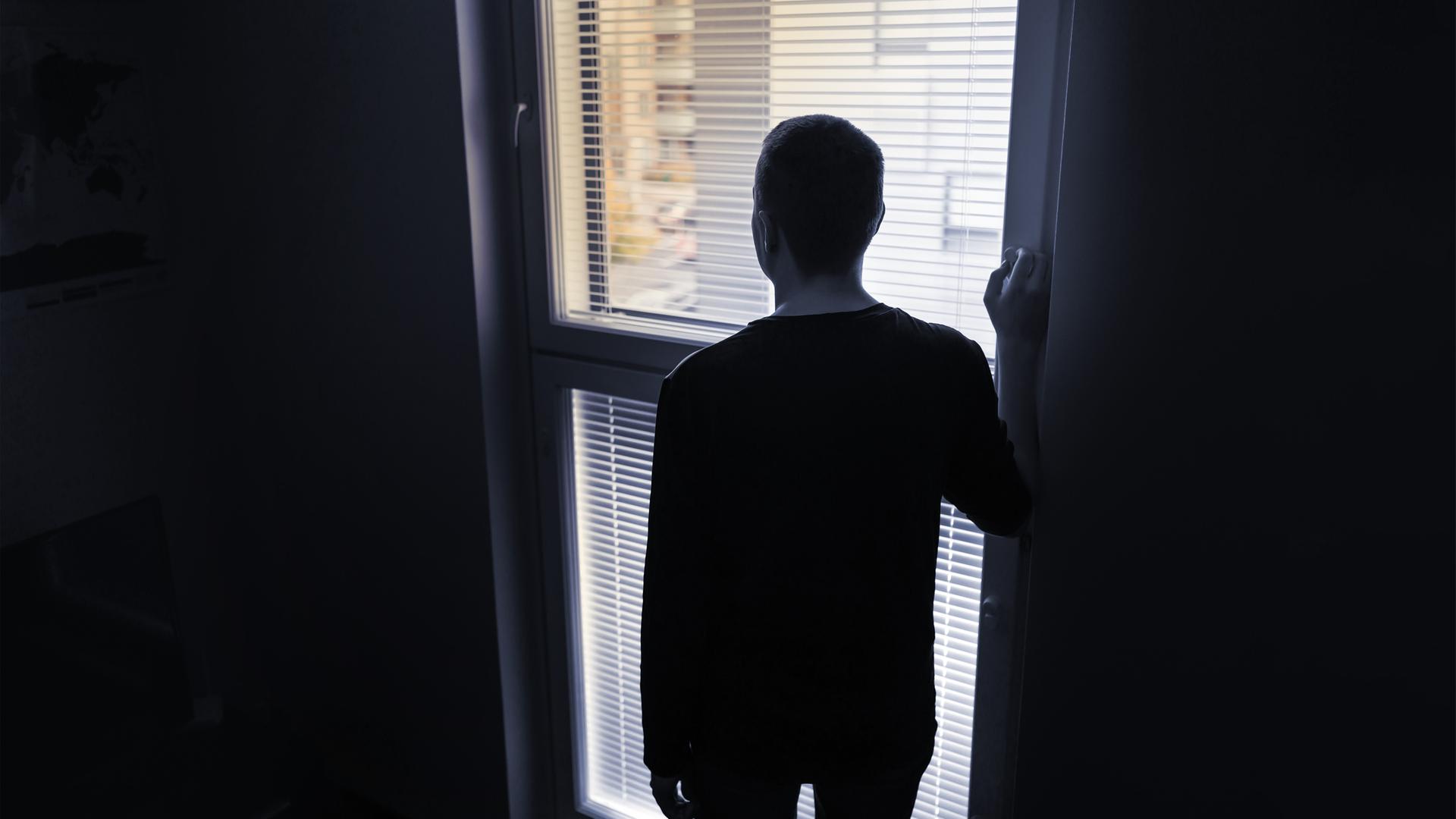 die Silhouette eines Mannes von hinten, der vor einem Fenster steht