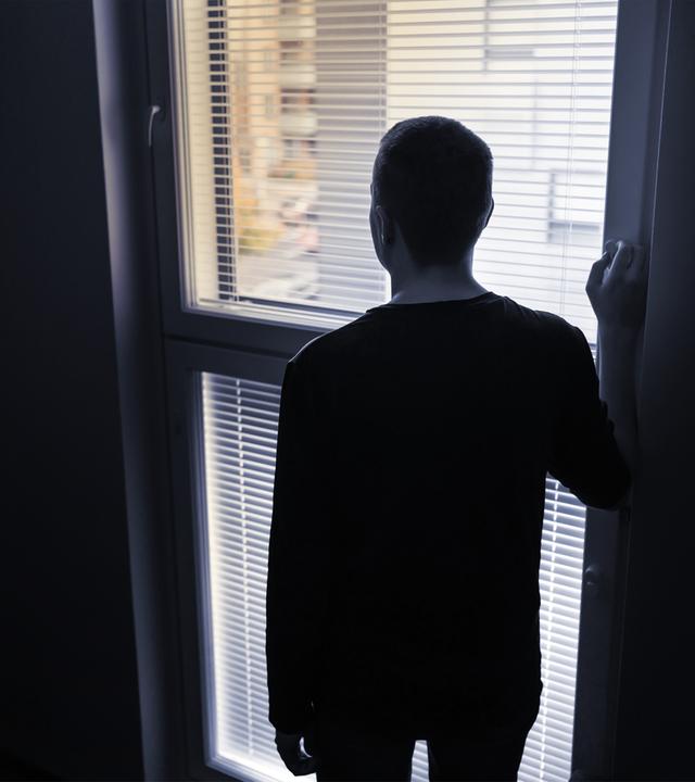 die Silhouette eines Mannes von hinten, der vor einem Fenster steht