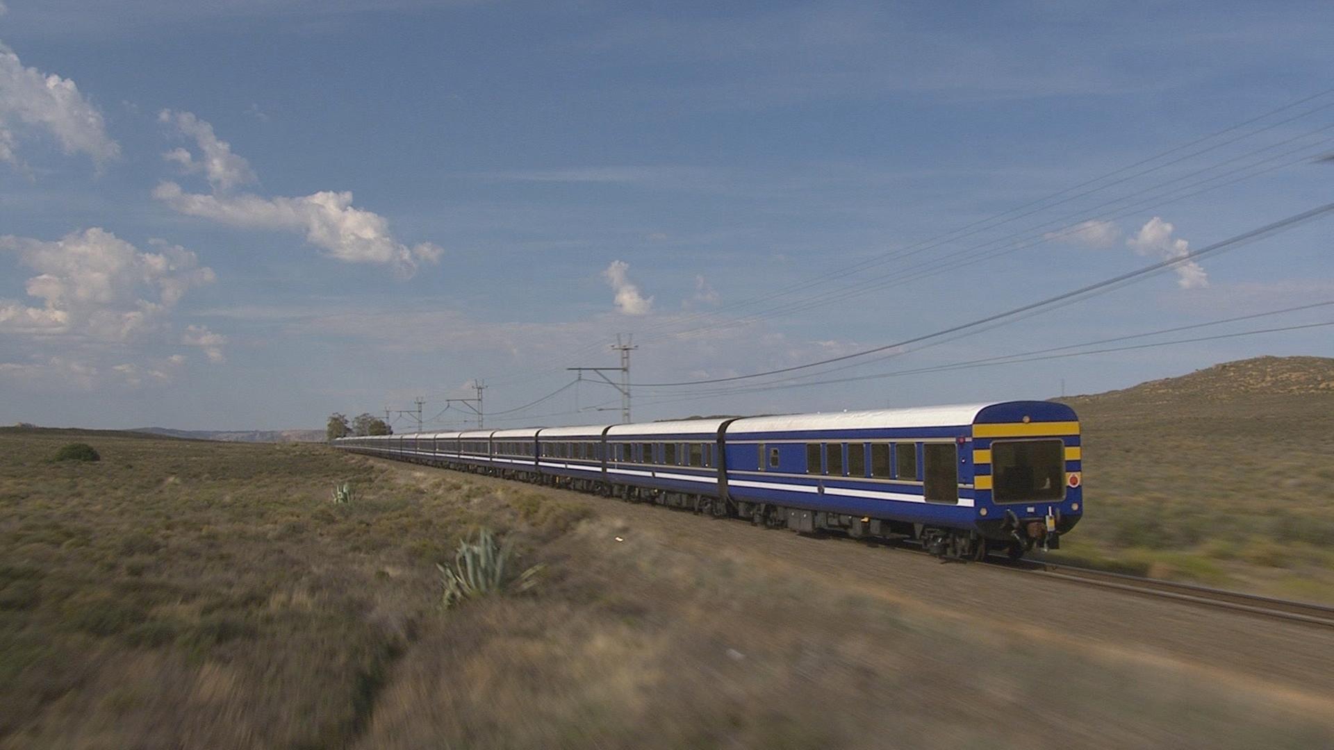  Ein blauer Zug fährt von links nach rechts in karger Landschaft.