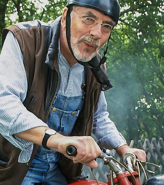 Peter sitzt mit etwas kritischem Blick und Helm auf einem Motorrad.