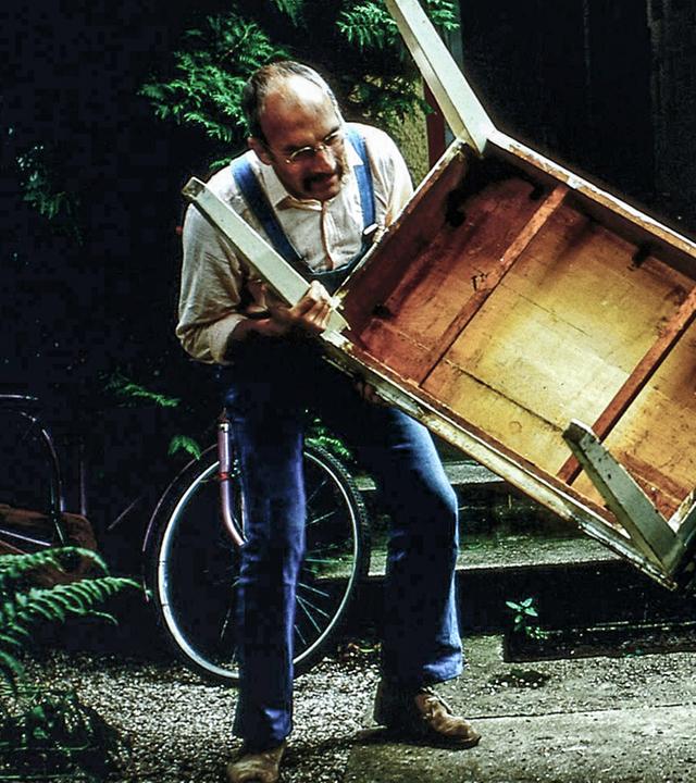 Peter Lustig trägt zusammen mit einer Frau einen schweren Tisch. Beide machen dabei eine krumme Figur.