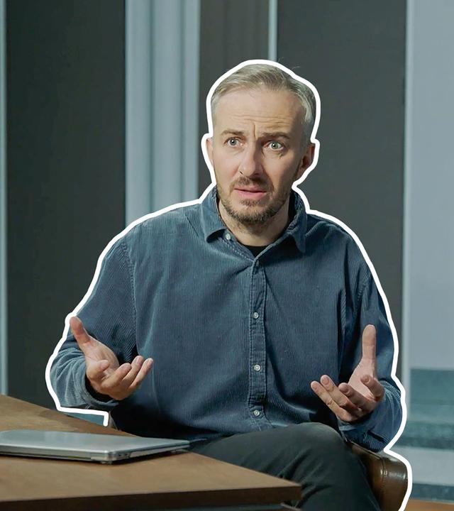 Jan Böhmermann sitzt am Schreibtisch.
