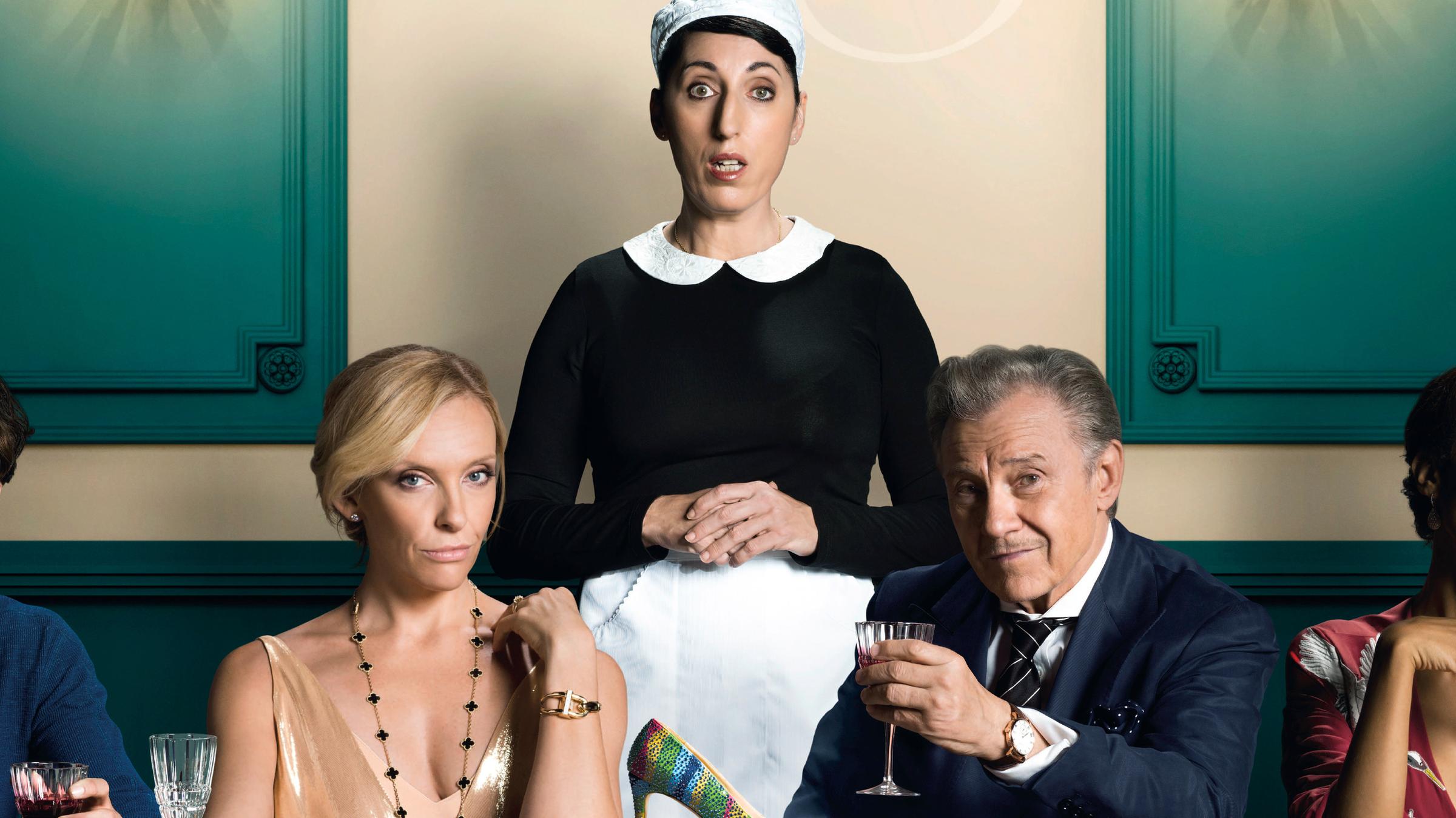 Anne (Toni Collette) und Bob (Harvey Keitel) sitzen in festlicher Kleidung an einem Tisch mit weiteren Gästen. Hinter ihnen beiden steht Maria (Rossy de Palma) in Dienstmädchenuniform. Alle drei schauen frontal in Richtung des Betrachters, Bob erhebt prostend ein Weinglas.
