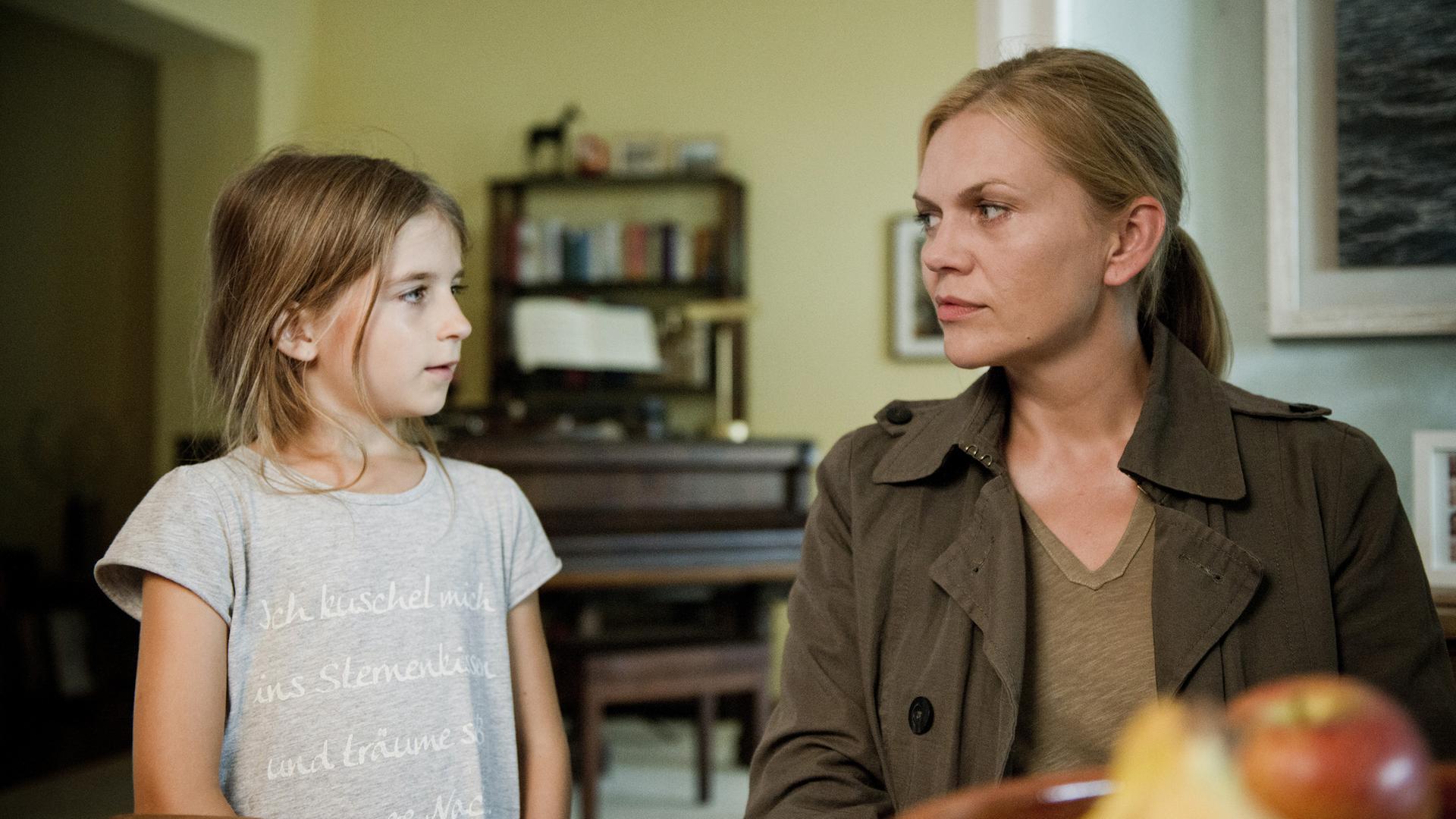 Elena Georgi (Milia Rütter) steht neben Helen Dorn (Anna Loos), die am Tisch sitzt.