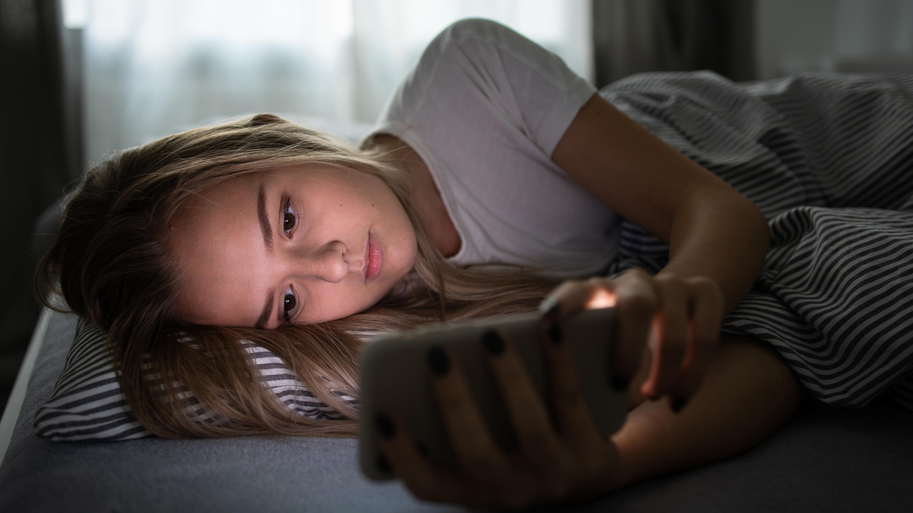 Mädchen liegt mit Smartphone im Bett