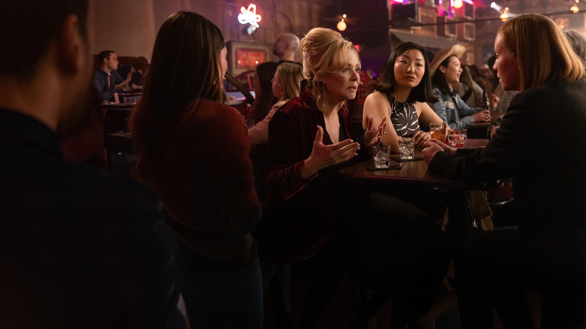 "Hacks - Mädelsabend, jung und alt": In einer belebten Bar: Deborah (Jean Smart) spricht ernst gestikulierend zu Ava (Hannah Einbinder), während Kiki (Poppy Liu) mit neutralem Gesichtsausdruck zu Ava schaut.