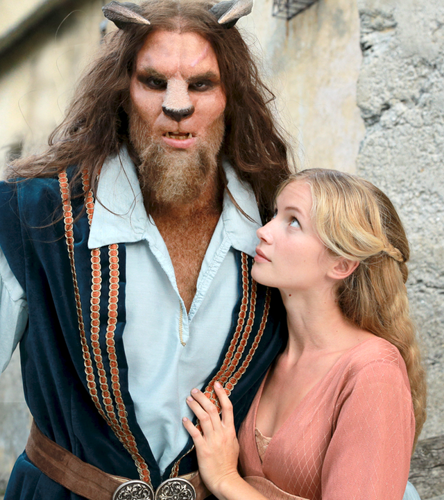 Vor den hohen Mauern einer Burg steht das Biest (Maximilian Simonischek) mit seiner tierisch breiten Nase, den raubtierhaften Eckzähnen, den Hörnern auf dem Kopf und in üppiger Behaarung. Rechts neben dem Biest und zärtlich an es geschmiegt, steht die schöne Elsa (Cornelia Gröschel).