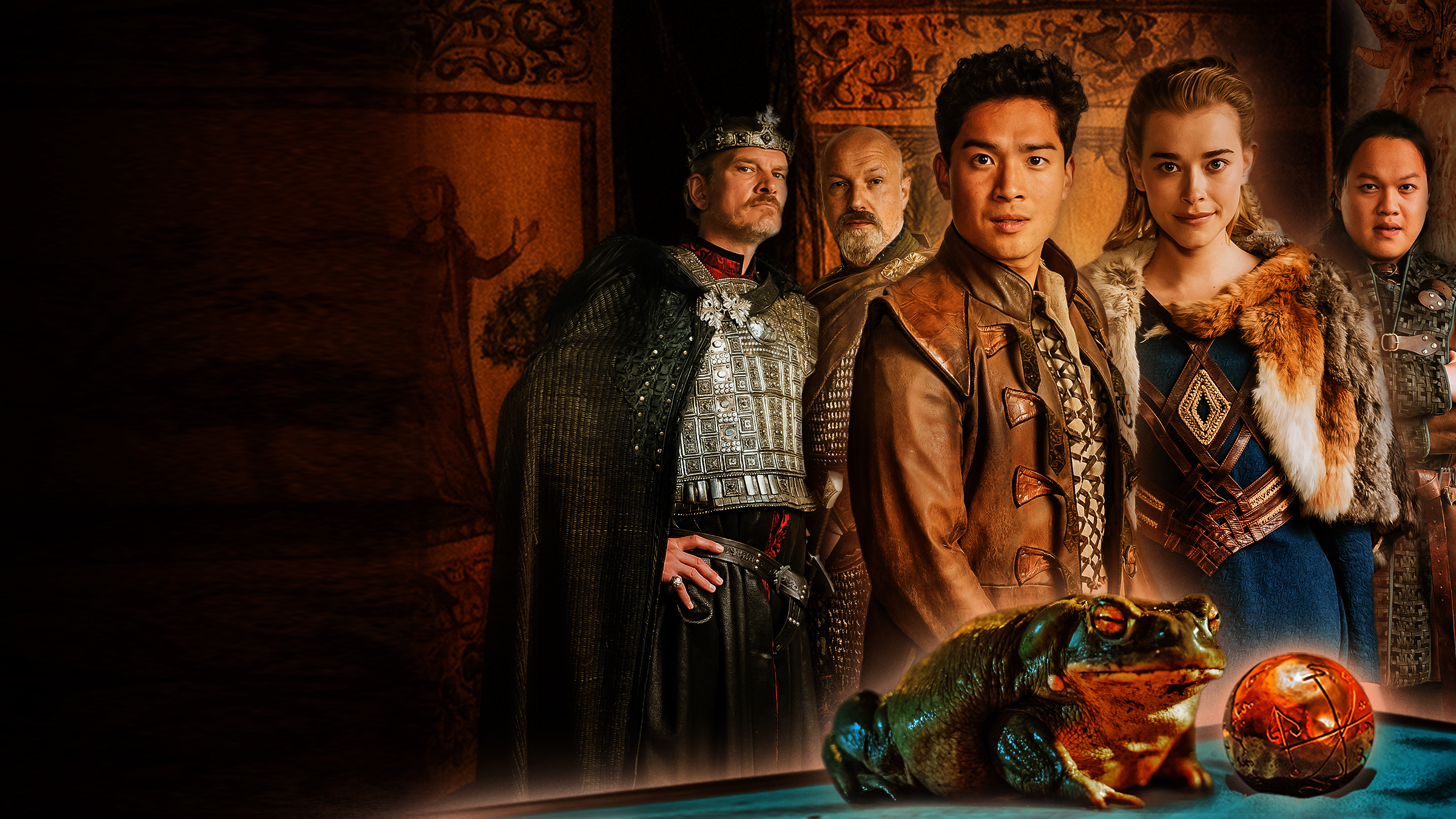 Sechs Personen in mittelalterlichen Gewändern schauen den Betrachter an. Von links: Neben einem groß gewachsenen älteren König, gespielt von Götz Otto, steht ein kräftiger Waffenmeister, gepielt von Simon Werner. Im Vordergrund in der Mitte präsentieren sich ein junger Prinz asiatischer Abstammung, verkörpert von Jan Liem, und eine blonde Prinzessin in einem blauen Kleid, dargestellt von Milena Tscharntke. Wieder etwas im Hintergrund sieht man einen jüngeren Mann mit schwarzen Haaren, gespielt von Anh Alexander Tran, und eine junge Frau mit kurzen blonden Haaren, verkörpert von Lea Drinda. Hinter ihnen sind braune bemalte Tücher gespannt. Ganz im Vordergrund sitzt ein Frosch neben einer goldenen Kugel.