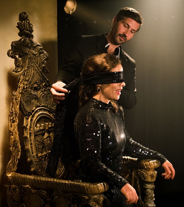 "Notruf Hafenkante - Magische Wahrheit": Kaya (Maya Haddad) sitzt auf einem Stuhl. Neben ihr steht ihr Mann Felix (Martin Loos), der gerade dabei ist, ihr die Augen zu verbinden.