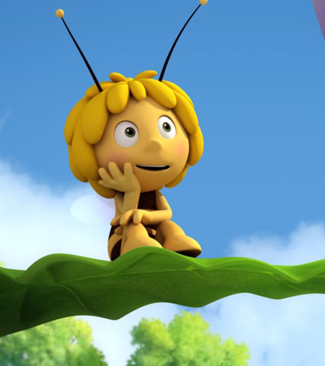 Maja feiert Schlüpftag und sitzt auf einem Blumenstengel mit ihrer Hand an den Kopf gestützt.