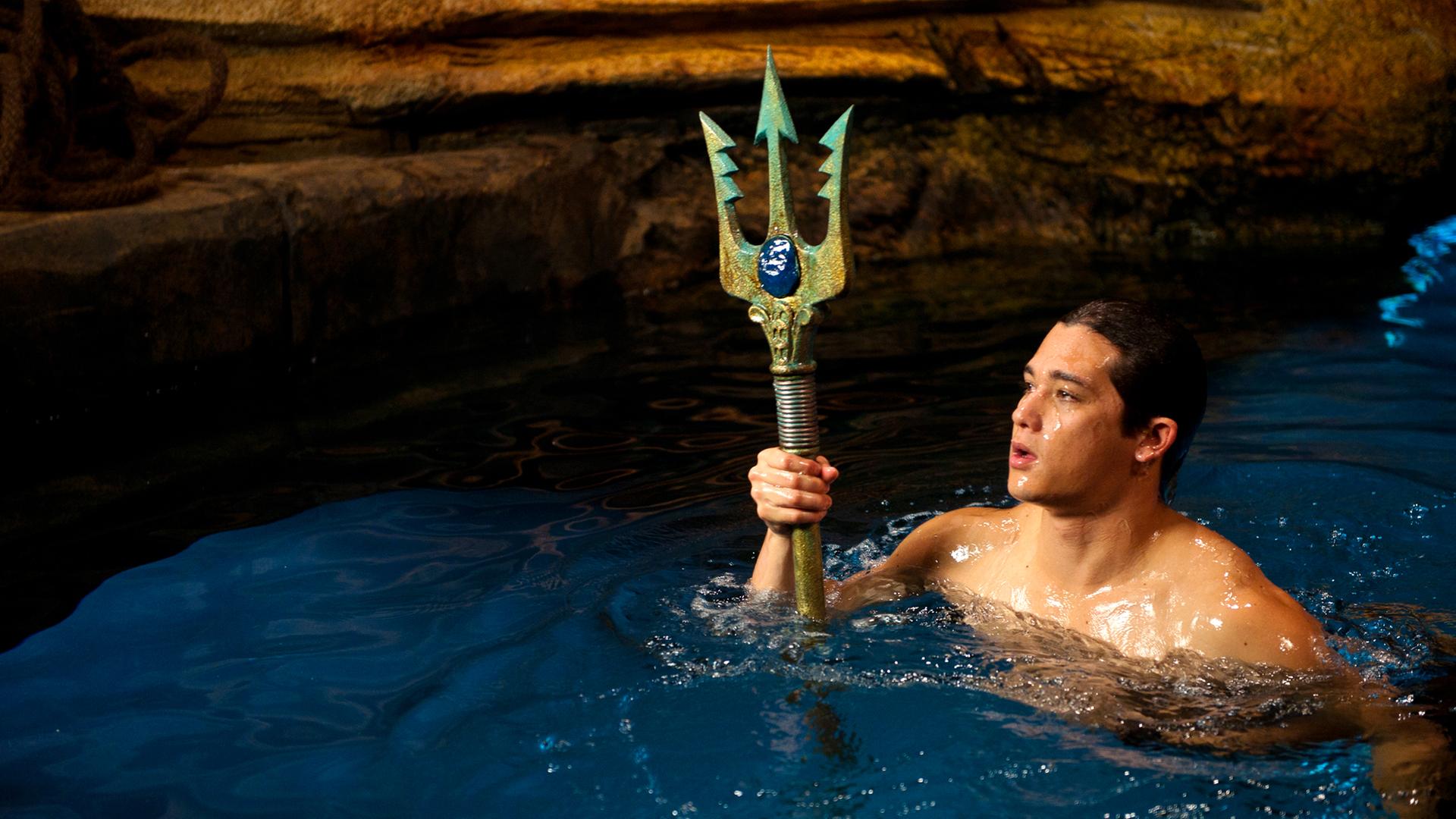 Zac schwimmt im Wasser der Grotte und hält den Dreizack in der Hand.