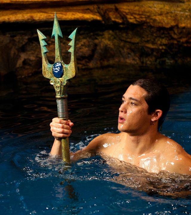 Zac schwimmt im Wasser der Grotte und hält den Dreizack in der Hand.
