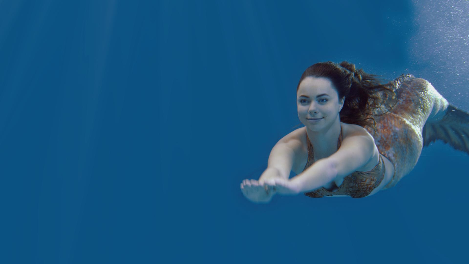 Die Meerjungfrau Nixie schwimmt zum Abkühlen durch tiefblaues Wasser nach Mako-Island.