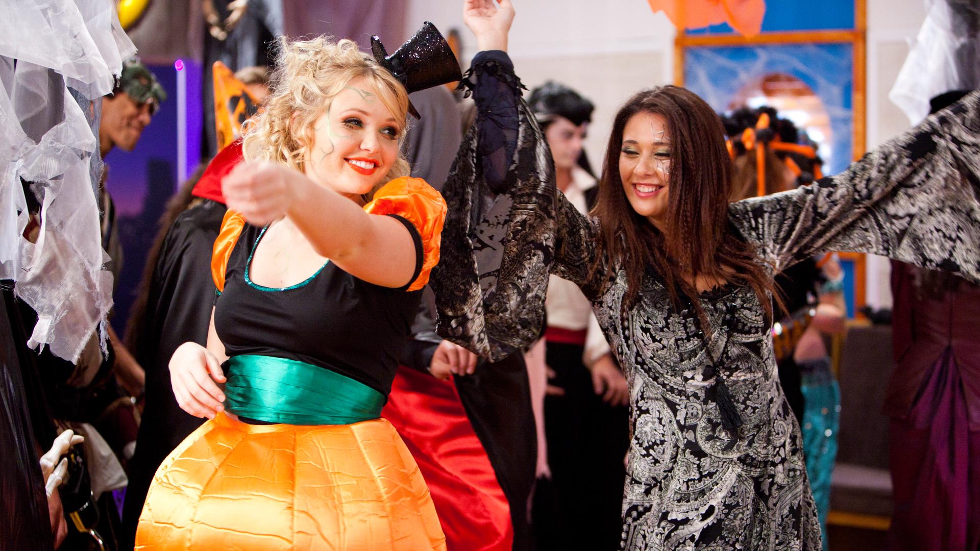 Carly, die als Kürbis verkleidet ist, und Evie, die ein Hexenkostüm trägt, tanzen auf der Halloween-Party im Ocean Café.
