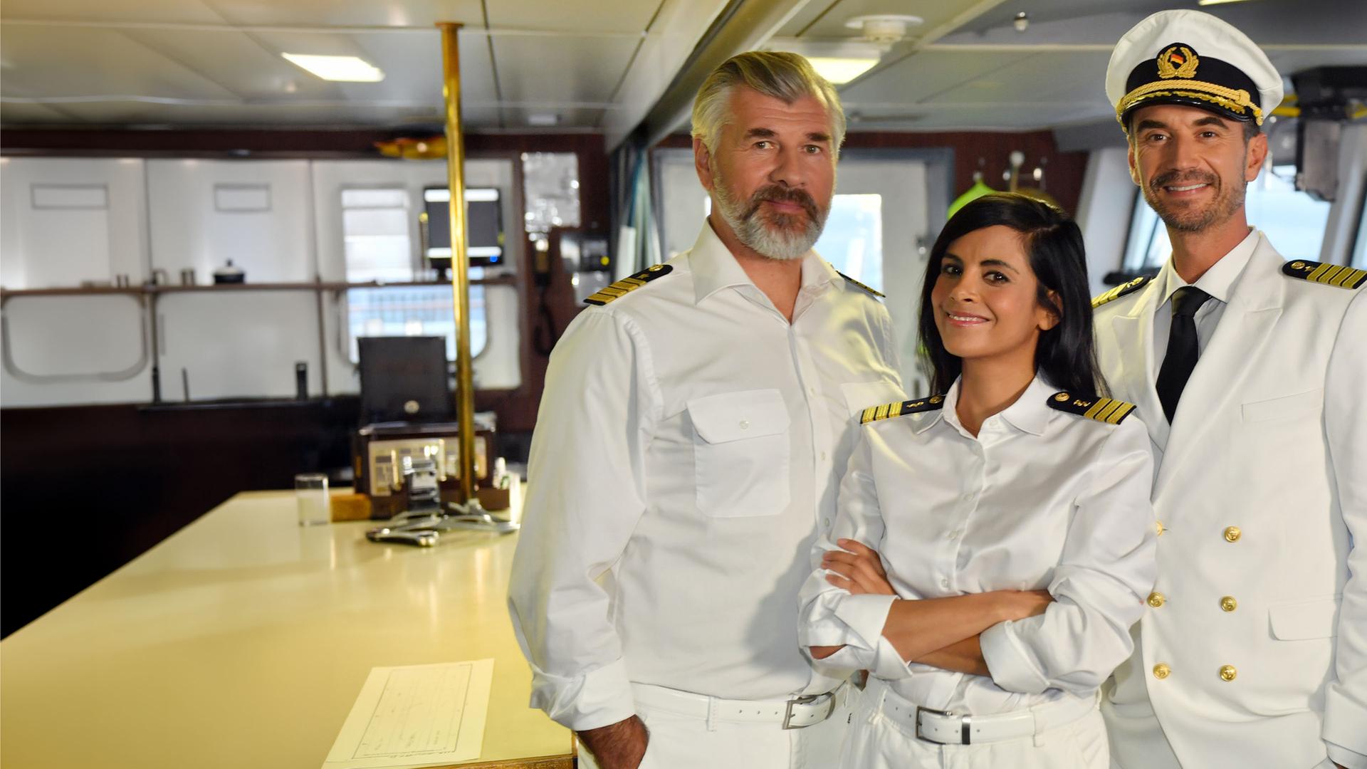 "Das Traumschiff: Malediven/Thaa Atoll": Dr. Jessica Delgado (Collien Ulmen-Fernandes) steht mit verschränkten Armen zwischen Kapitän Max Parger (Florian Silbereisen) und Staffkapitän Martin Grimm (Daniel Morgenroth) auf der Kommandobrücke. Alle drei tragen ihre Uniformen und lächeln in die Kamera.
