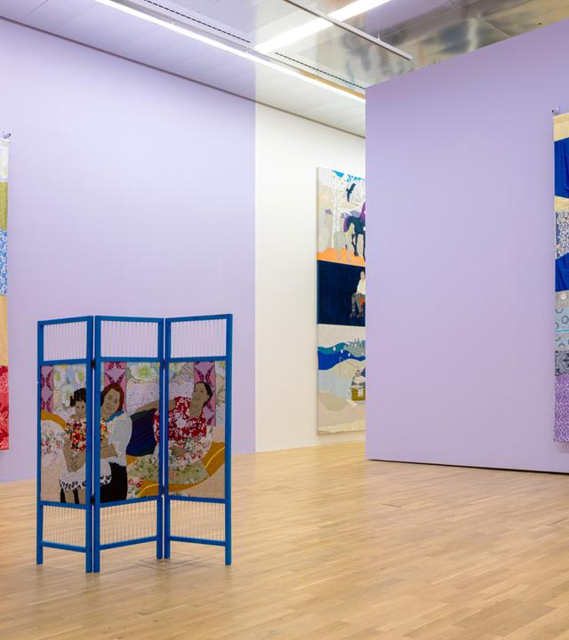 In einer Ausstellungshalle hängen zwei Gemälde, die jeweils eine Frau zeigen. Im Raum steht ein bemalter Paravent.