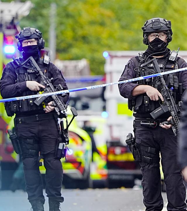 Bewaffnete Sicherheitskräfte hinter Absperrband neben Rettungswagen.