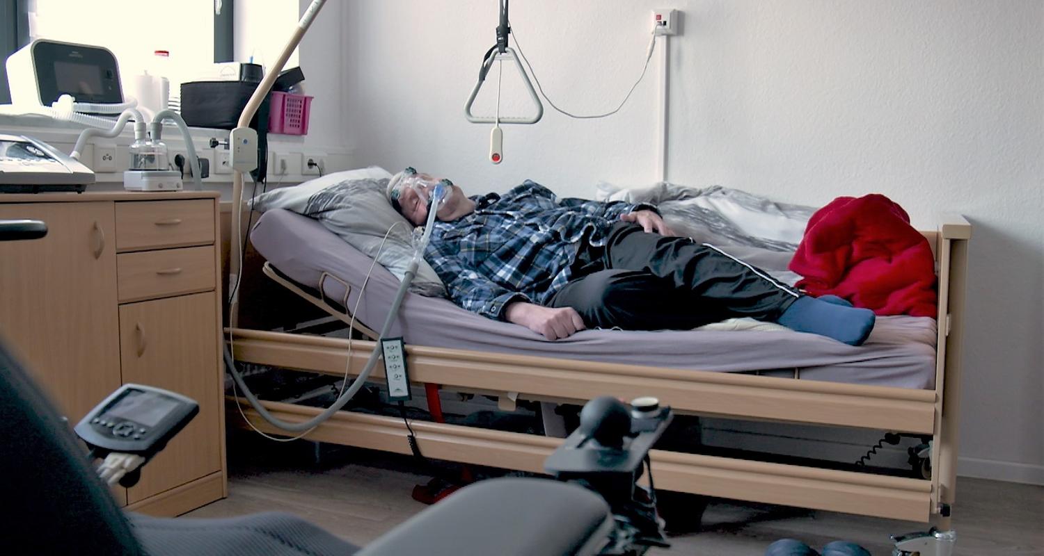 Beatmeter Mann liegt zu Hause im Krankenbett im Vordergrund Elektrorollstuhl