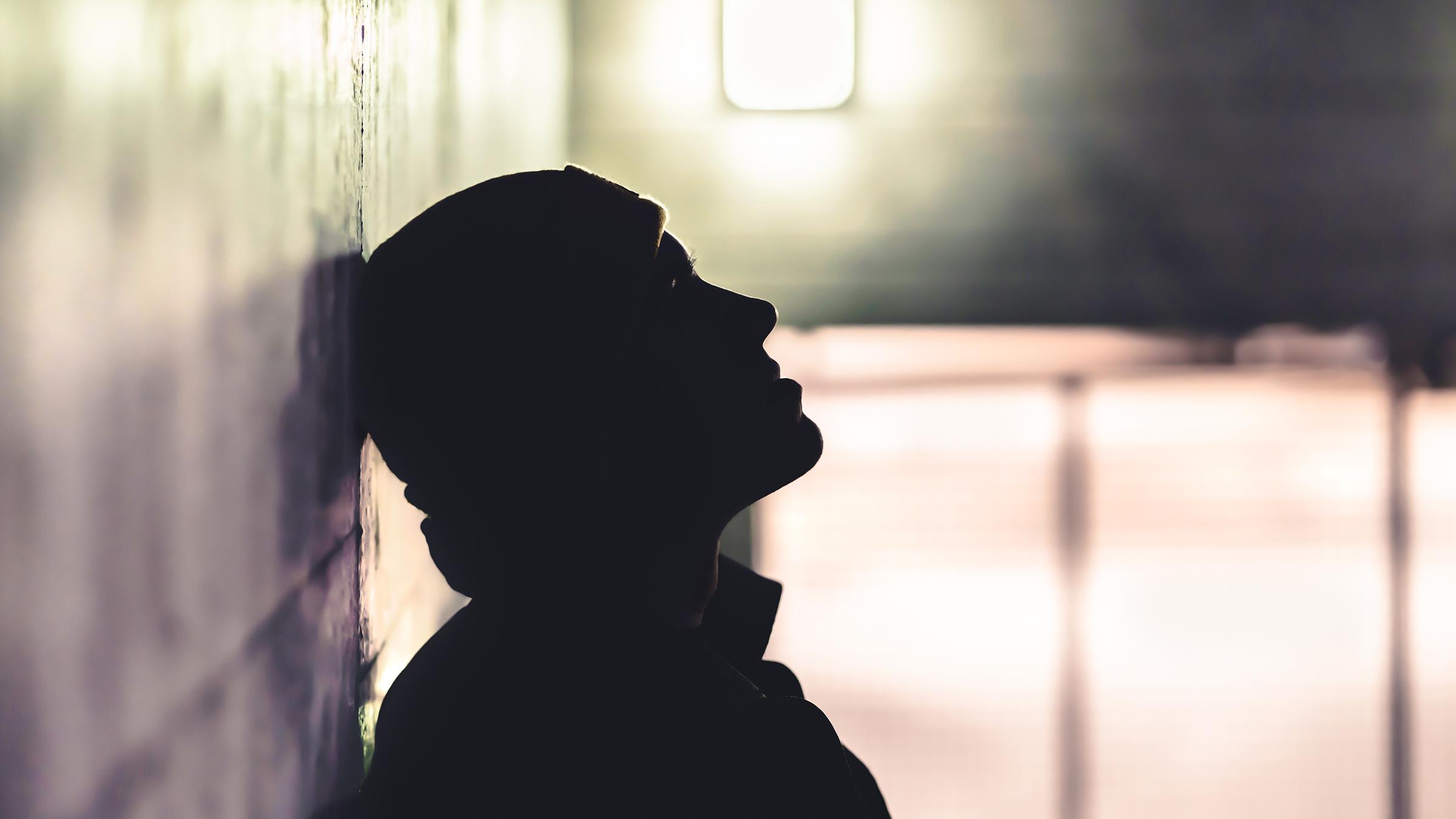 Eine Person lehnt in einem düsteren Raum mit dem Kopf an der Wand.