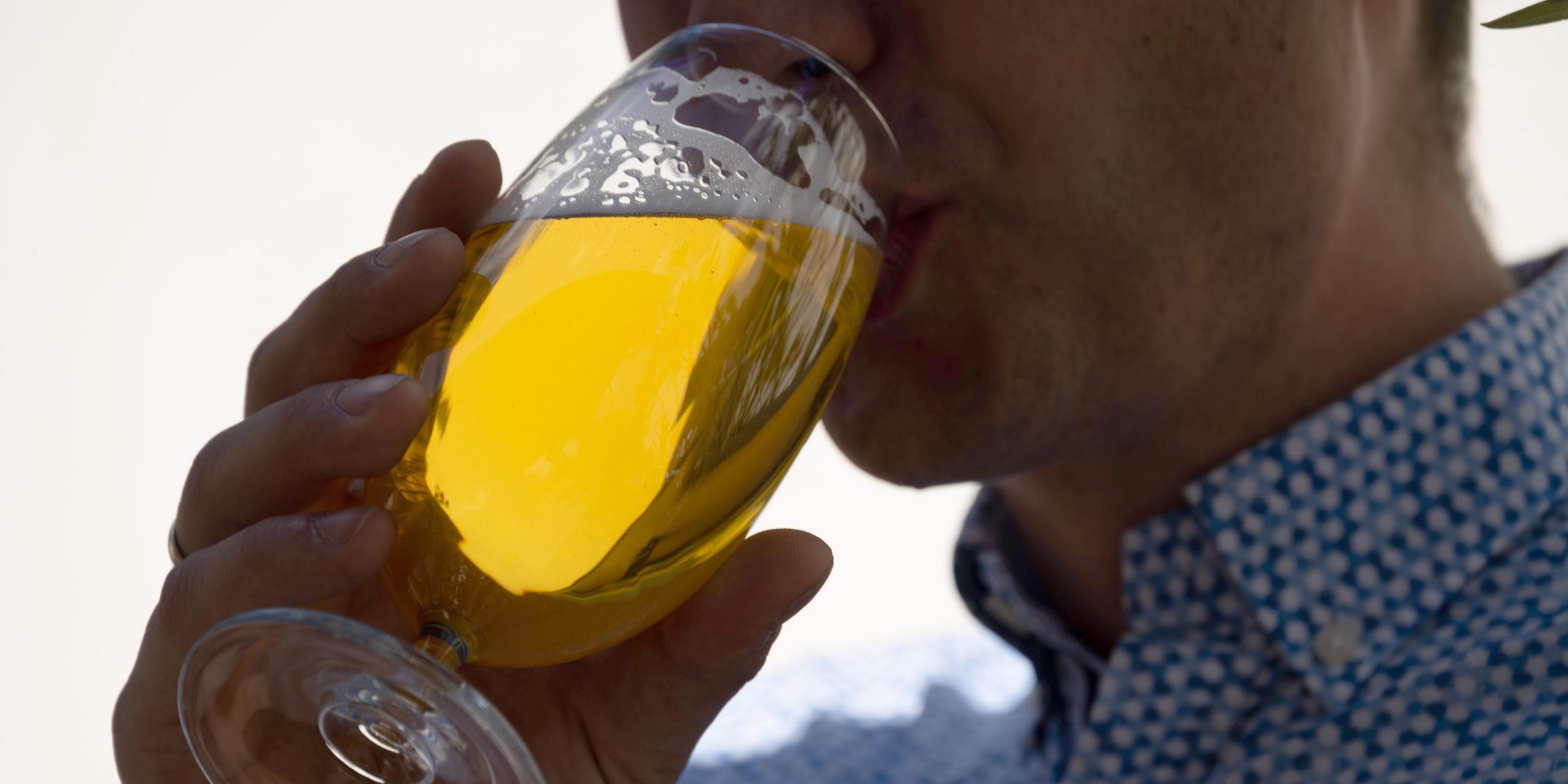 Eine Mann hält ein Glas mit frischem Bier in der Hand und nimmt einen Schluck davon