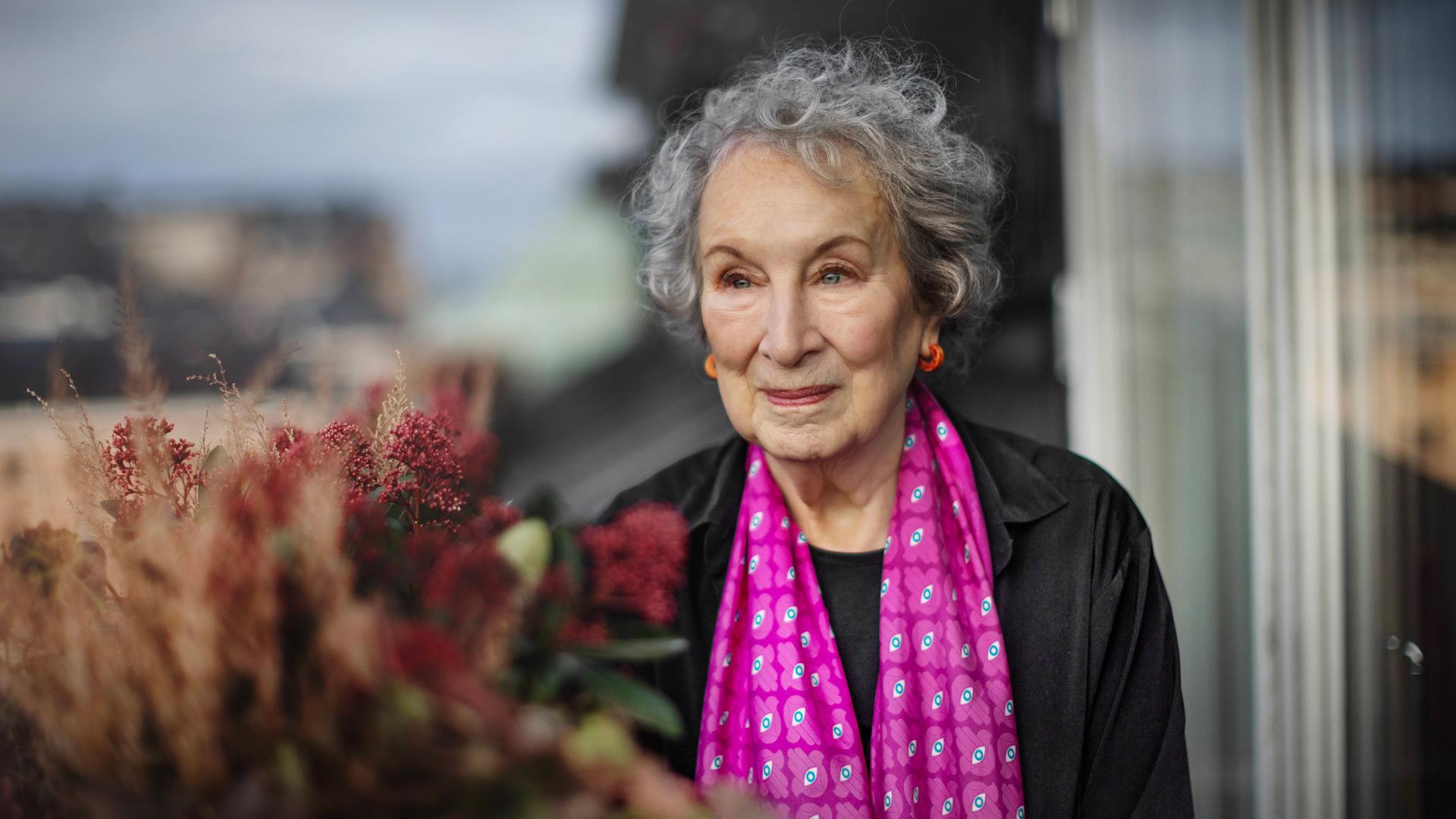 Porträtfoto einer älteren Frau mit grauen Locken, die einen gemusterten pinkfarbenen Schal umgehängt hat.