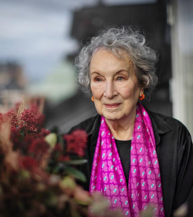 Porträtfoto einer älteren Frau mit grauen Locken, die einen gemusterten pinkfarbenen Schal umgehängt hat.