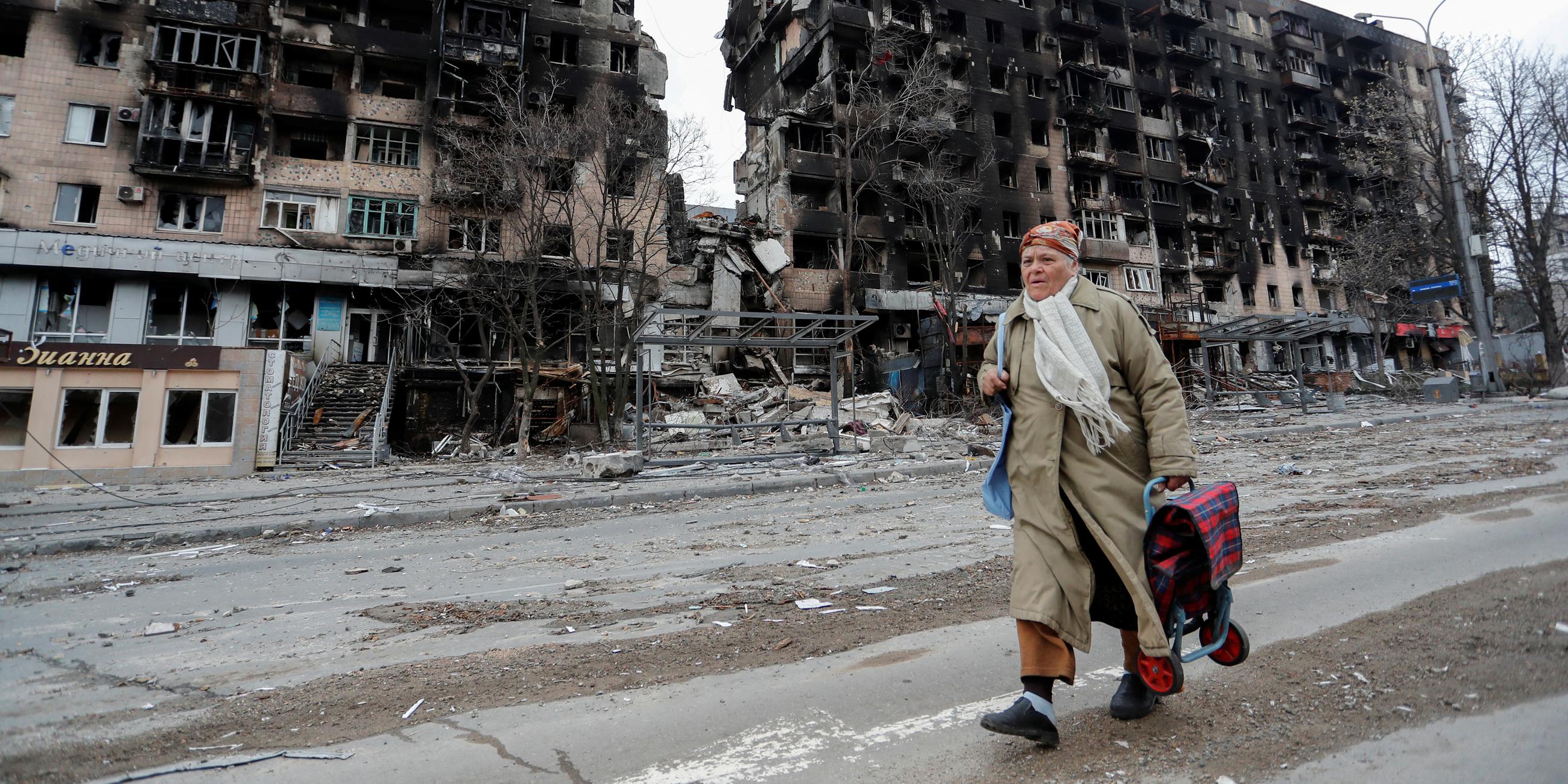 Eine Passantin geht an zerstörten Gebäuden in Mariupol vorüber. 