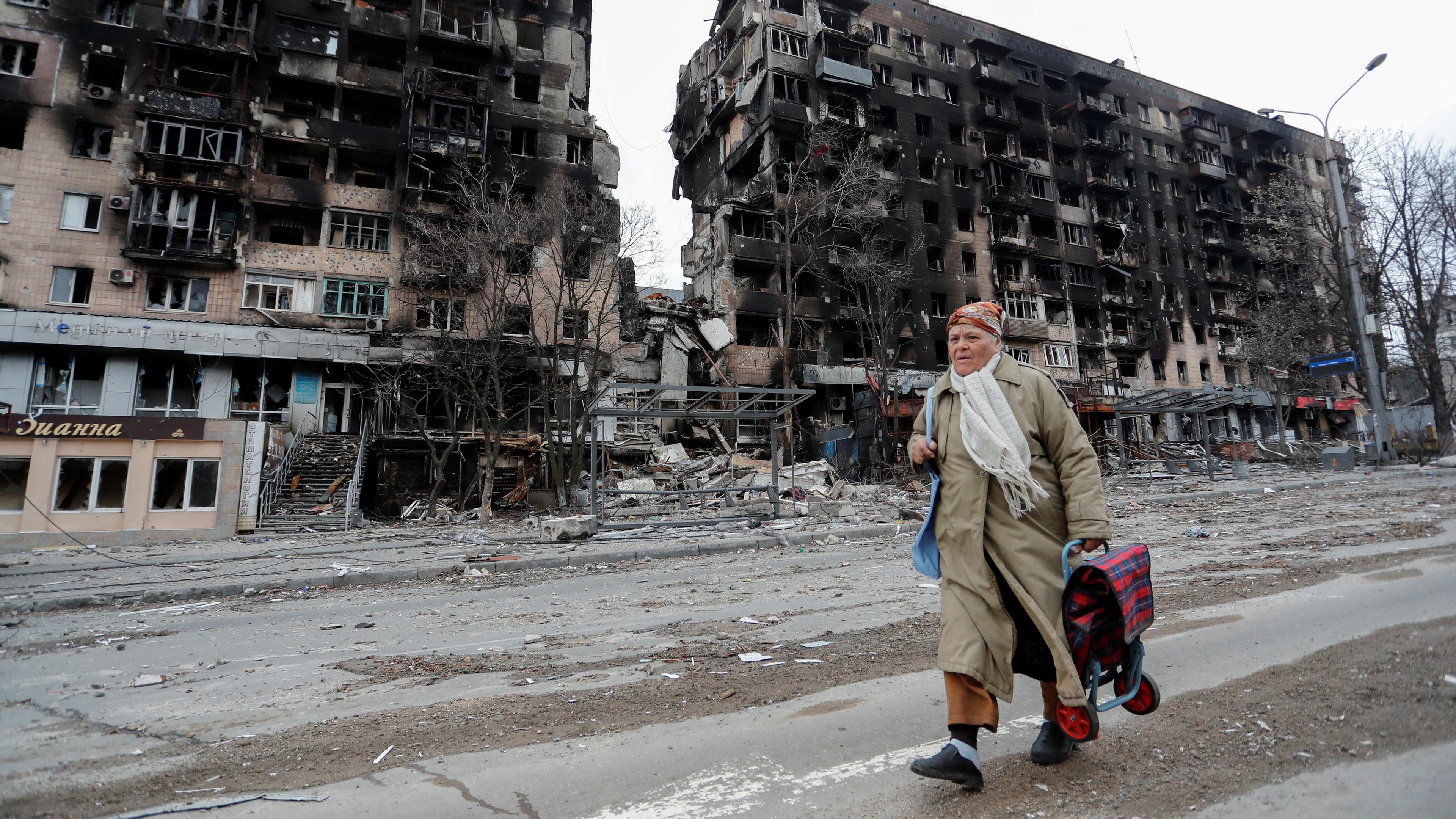 Eine Passantin geht an zerstörten Gebäuden in Mariupol vorüber. 