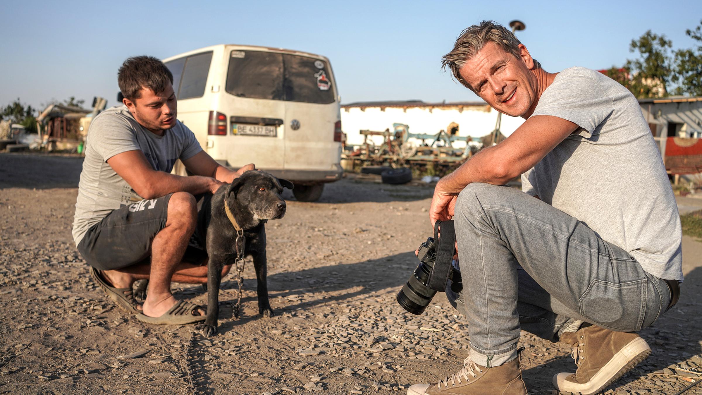 "Markus Lanz: Ukraine - Leben mit dem Krieg": Der Bauer Vitaliy und Markus Lanz sitzen in der Hocke auf einer Straße. Vitaliy streichelt seinen Hund, während Markus Lanz in die Kamera sieht.