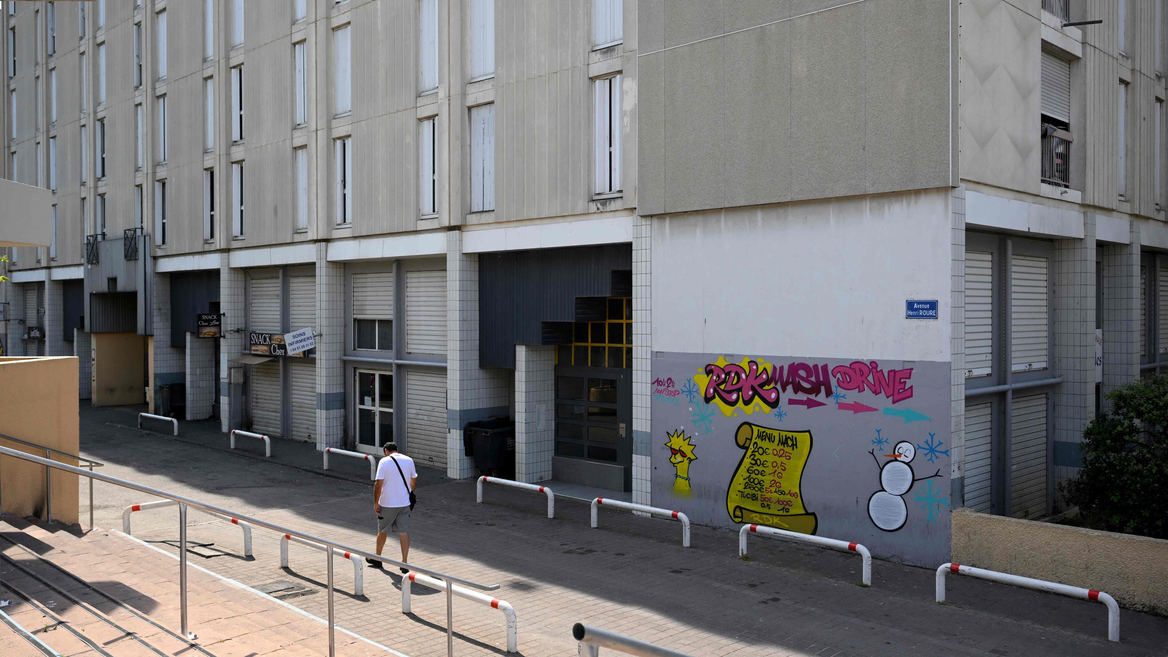 Ein Mann läuft an einem Gebäude in Marseille vorbei, auf dem ein Graffiti ist. 