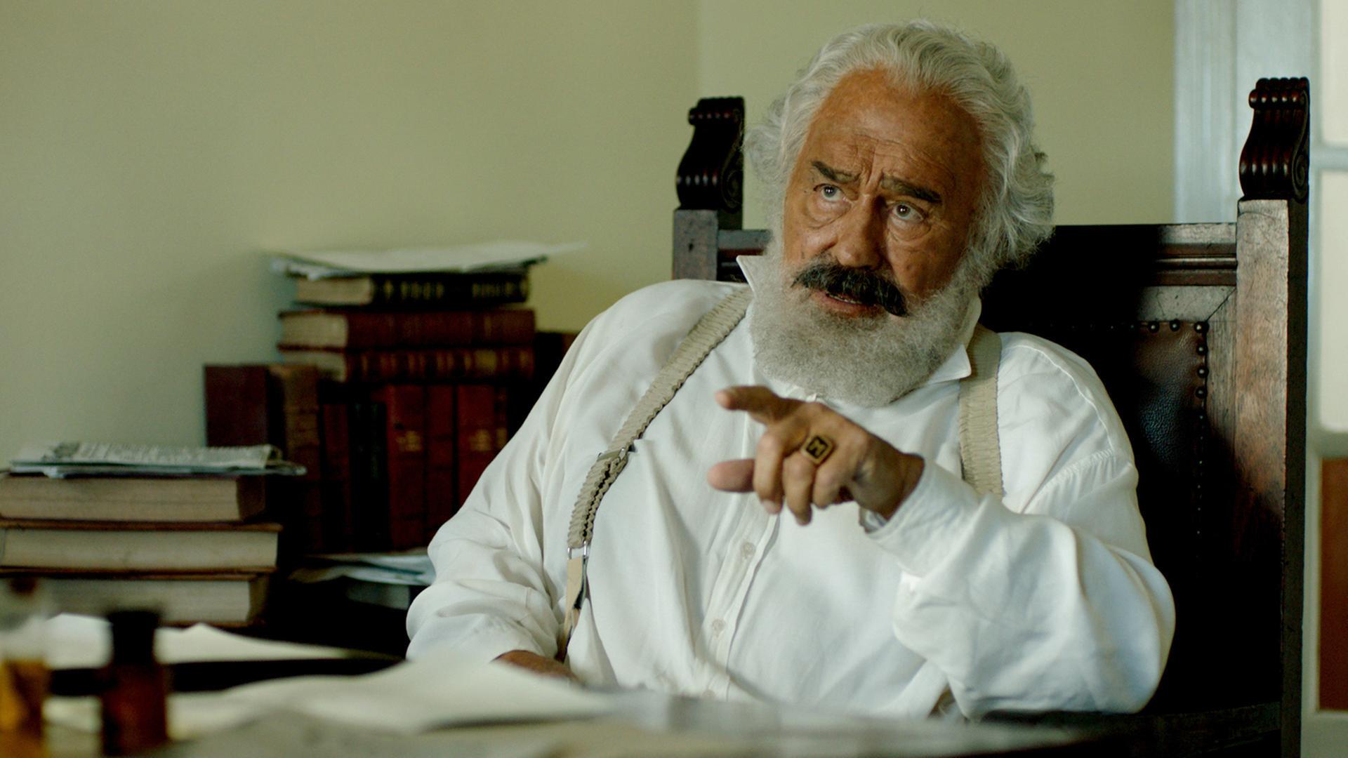 Karl Marx (Mario Adorf) sitzt an seinem Schreibtisch 