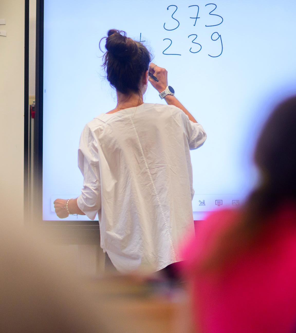 Eine Lehrerin schreibt eine Mathematikaufgabe auf eine digitale Schultafel im Klassenraum einer 4. Klasse einer Grundschule, aufgenommen am 17.08.2023