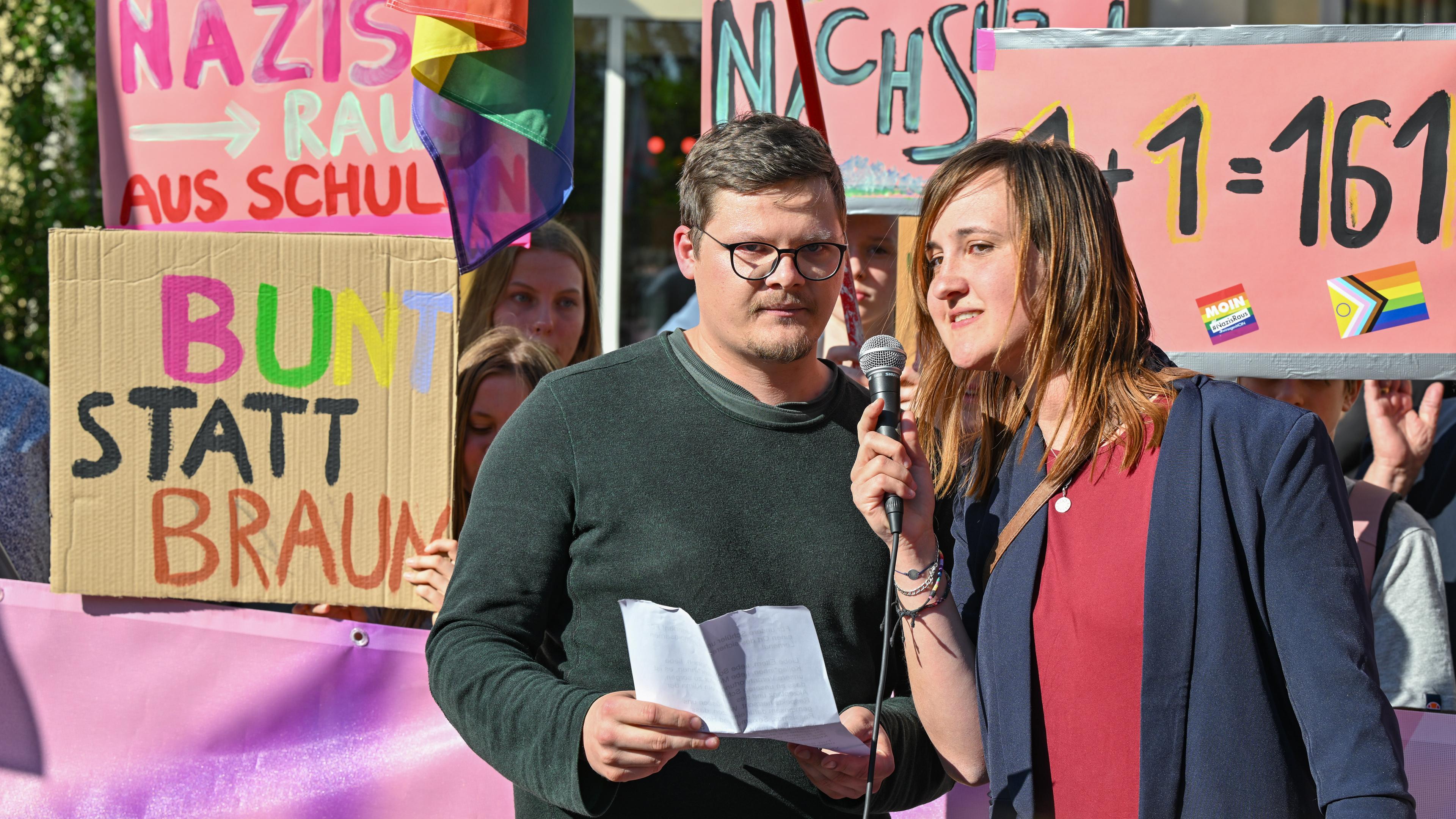Der Lehrer Max Teske und seine Kollegin Laura Nickel bei einer Kundgebung. Im Hintergrund Plakate.
