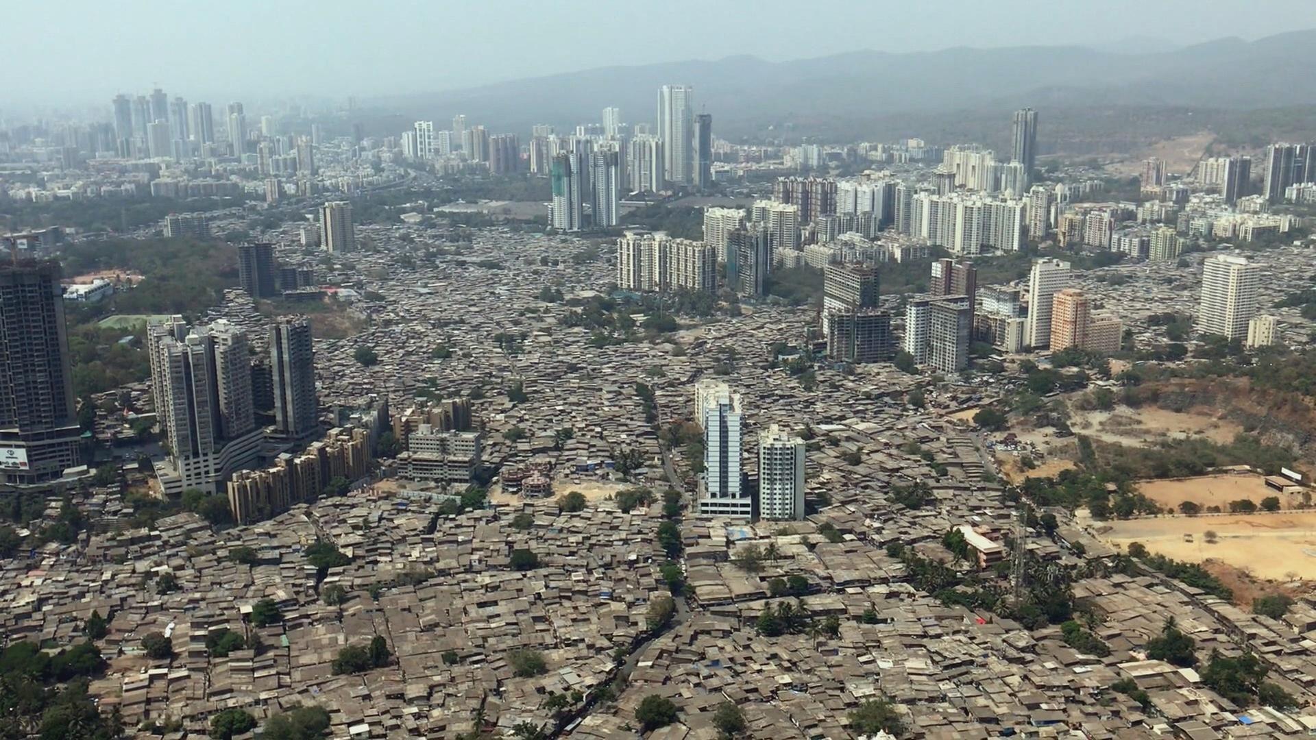 Luftaufnahme Mumbai: Zwischen vielen Hochhäusern ist eine große Fläche mit flachen Häusern zu sehen.
