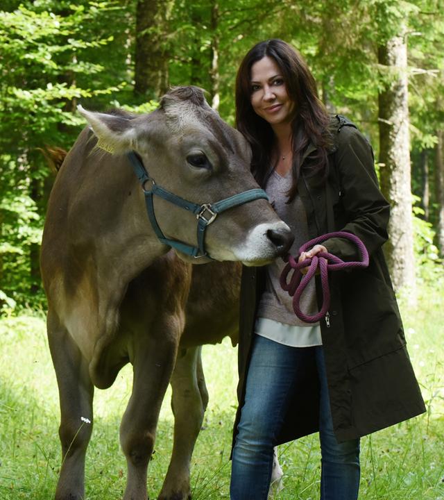 "Frühling - Mehr als Freunde": Dorfhelferin Katja (Simone Thomalla) steht auf einer Waldlichtung, hält eine Kuh am Zaumzeug fest und lächelt.