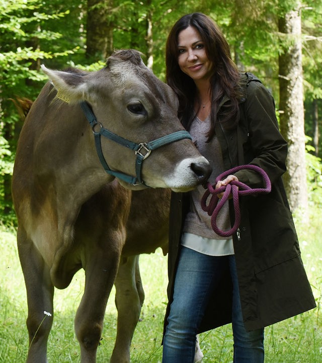 "Frühling - Mehr als Freunde": Dorfhelferin Katja (Simone Thomalla) steht auf einer Waldlichtung, hält eine Kuh am Zaumzeug fest und lächelt.
