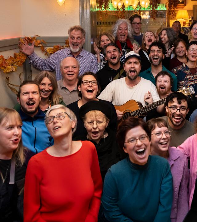 Eine Gruppe befindet sich singend in einem Wirtshaus, in der Mitte David mit Gitarre, Halbtotale.