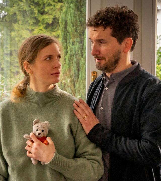 Steffi hält in ihrer linken Hand einen gehäkelten Teddybären, den sie an ihren Oberkörper drückt.