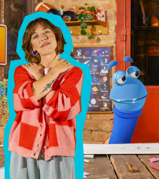 Singa sitzt mit Kopfverband an einem Tisch, das SingDing schaut sie an. Eine Frau steht neben ihnen und umarmt sich. 