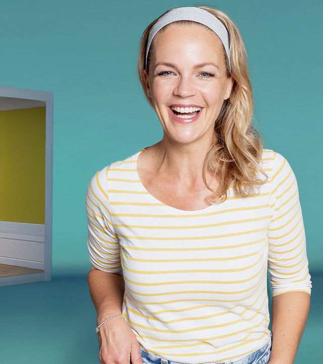 Eva Brenner, lachend, vor blauem Hintergrund. Links von ihr die Animation eines Schlafzimmers mit Bett, Nachttisch und Teppich.